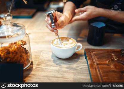 Male barista makes drawing with foam, coffee making. Professional cappuccino preparation by barman, wooden counter on background. Barista makes drawing with foam, coffee making