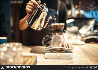 Male barista pours boiling water into the glass with coffee, cafe counter on background. Professional espresso preparation by barman in cafeteria, bartender occupation. Male barista pours boiling water into the glass
