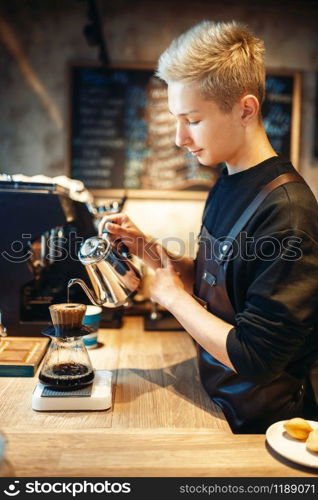 Male barista pours boiling water into the glass with coffee, cafe counter on background. Professional espresso preparation by barman in cafeteria, bartender occupation. Male barista pours boiling water into the glass