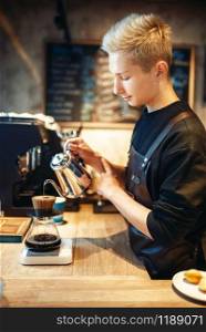 Male barista pours boiling water into the glass with coffee, cafe counter on background. Professional espresso preparation by barman in cafeteria, bartender occupation. Male barista pours boiling water into the glass