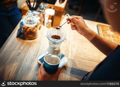 Male barista pours ground coffee into the glass standing on the stove. Barman works in cafeteria, bartender occupation. Male barista pours ground coffee into the glass