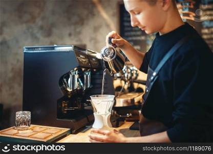 Male barista pours hot water into the glass with coffee, cafe counter and espresso machine on background. Barman works in cafeteria, bartender occupation. Barista pours hot water into the glass with coffee