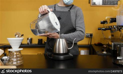 male barista with medical mask pouring water kettle