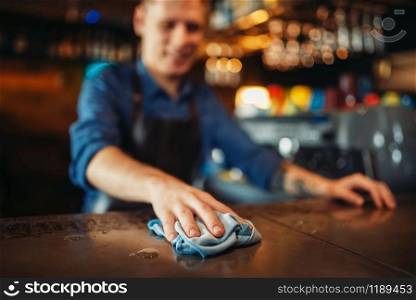 Male barman in apron cleans bar counter. Barkeeper occupation, bartender puts things in order. Barman in apron cleans bar counter after party
