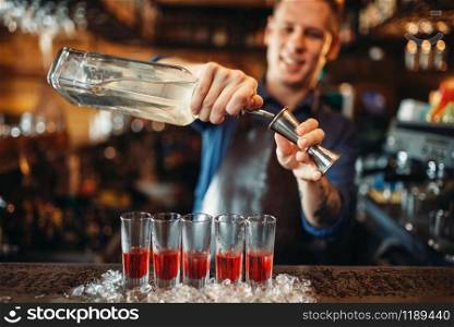 Male barman in apron prepares alcoholic coctail, glasses standing in ice. Bartender at the bar counter in pub. Barkeeper occupation. Male barman in apron prepares alcoholic coctail