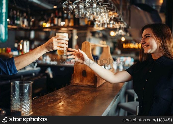 Male barman passes a glass of beer to female visitor. Barkeeper occupation, bartender and woman at the bar counter. Male barman passes glass of beer to female visitor
