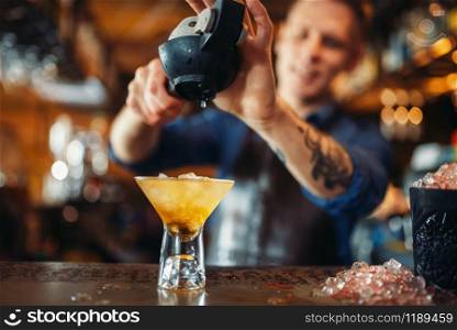 Male barman squeezes lemon into the glass full of ice. Barkeeper occupation, bartender at the bar counter. Barman squeezes lemon into the glass full of ice