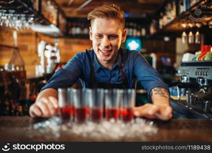 Male bartender in apron prepares four beverages in a glasses. Barman at the bar counter in pub. Barkeeper occupation. Male bartender prepares four beverages in glasses