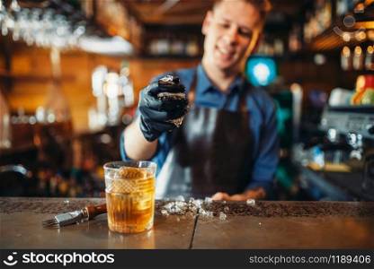 Male bartender in apron works with ice at the bar counter. Alcohol beverage preparation. Barman occupation. Male bartender works with ice at the bar counter