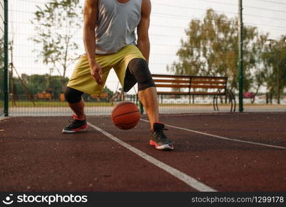 Male basketball player with ball shows his skill on outdoor court. Male athlete in sportswear on streetball training, summer stadium