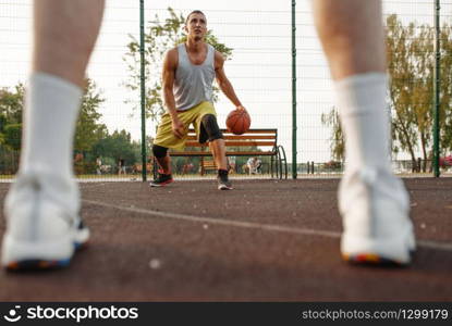 Male basketball player with ball shows his skill on outdoor court. Male athlete in sportswear on streetball training, summer stadium. Male basketball player with ball shows his skill