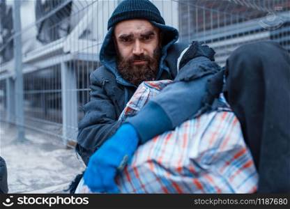 Male bearded beggar lies on city street. Poverty is a social problem, homelessness and loneliness, alcoholism and drunk addiction, urban lonely. Male bearded beggar lies on city street