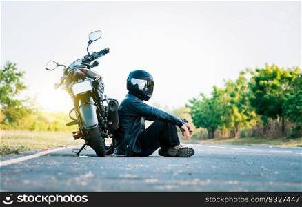 Male biker sitting next to his motorcycle on the road. Male motorcyclist sitting and leaning on his motorcycle on the asphalt