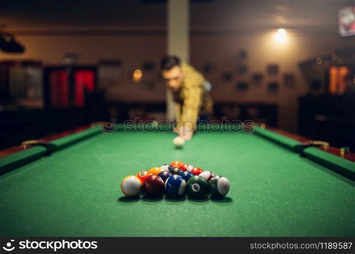 Male billiard player with cue aiming at the table with colorful balls. Man plays american game in sport bar. Male billiard player with cue aiming at the table