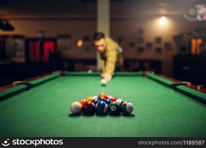 Male billiard player with cue aiming at the table with colorful balls. Man plays american game in sport bar. Male billiard player with cue aiming at the table