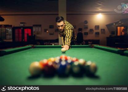 Male billiard player with cue aiming at the table with colorful balls. Man plays american pool game in sport bar