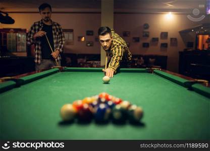 Male billiard player with cue aiming at the table with colorful balls. Man plays american pool game in sport bar. Male billiard player with cue aiming at the table