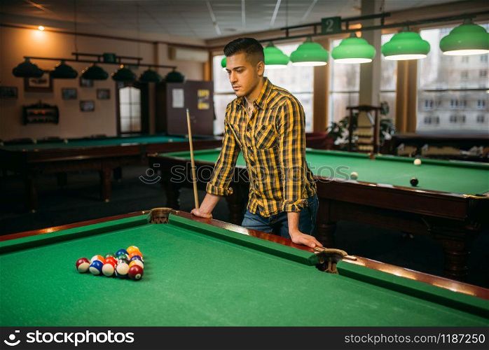 Male billiard player with cue at the green table with colorful balls, poolroom interior on background. Man plays american pool game in sport bar