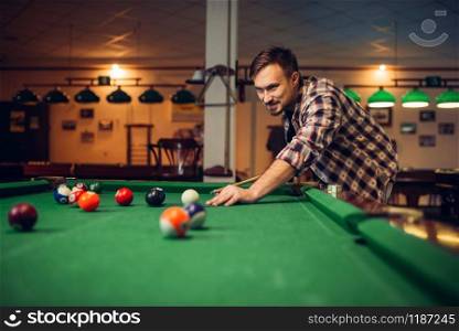 Male billiard player with cue at the table with colorful balls. Man plays american pool game in sport bar. Male billiard player with cue at the table