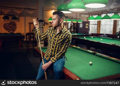 Male billiard player with cue poses at the green table. Man plays american pool game in sport bar. Male billiard player with cue poses at the table