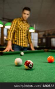 Male billiard player with cue, view from the table with colorful balls, poolroom interior on background. Man plays american pool game in sport bar. Male billiard player with cue, view from the table