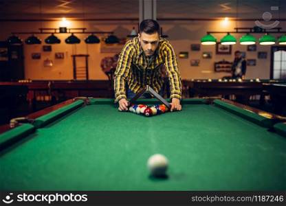 Male billiard player with pyramid places colorful balls on green table. Man plays american pool game in sport bar