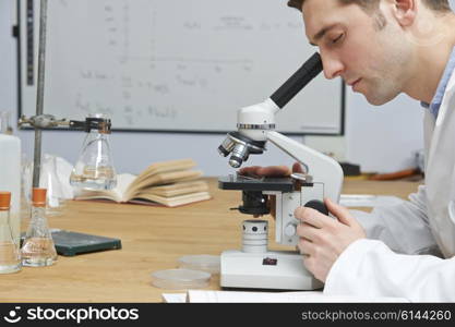 Male Biology Teacher Looking Through Microscope In Classroom