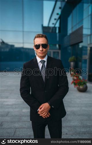 Male bodyguard in suit and sunglasses outdoors. Guarding is a risky profession. Professional guard, politician persons and businesspeople safeguard, safe control. Male bodyguard, politician persons safeguard