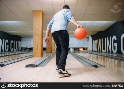 Male bowler standing on lane and poses with ball in hands, back view. Bowling alley player prepares to throw strike shot in club, active leisure. Male bowler standing on lane and poses with ball