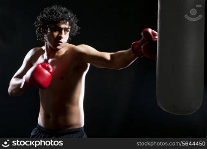 Male boxer hitting heavy bag over black background
