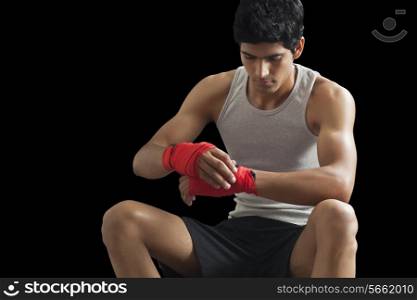 Male boxer taping up hands isolated over black background