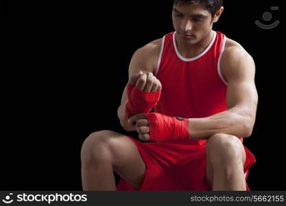 Male boxer taping up hands over black background