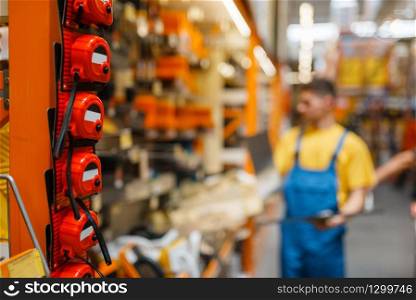 Male builder at the shelf with tools in hardware store. Constructor in uniform look at the goods in diy shop