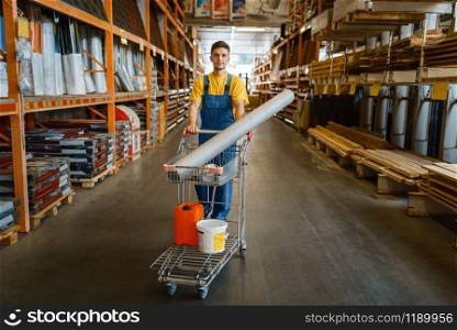 Male builder carries building materials in a cart, hardware store. Customer look at the goods in diy shop. Male builder carries building materials in a cart
