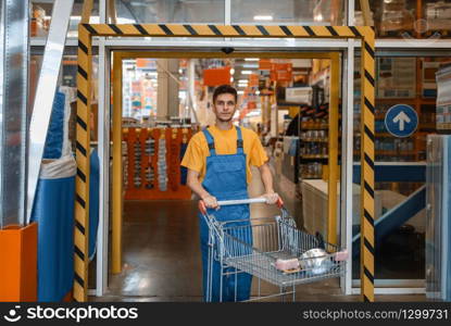 Male builder carries building materials in a cart, hardware store. Customer look at the goods in diy shop. Male builder carries building materials in a cart