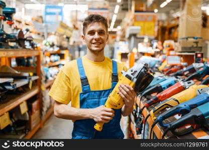 Male builder choosing angle grinder at the shelf in hardware store. Constructor in uniform look at the goods in diy shop