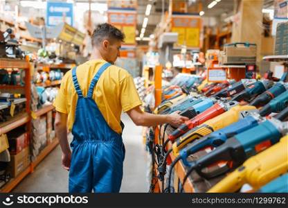 Male builder choosing angle grinder at the shelf in hardware store. Constructor in uniform look at the goods in diy shop. Builder choosing angle grinder in hardware store