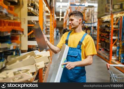 Male builder choosing screed level in hardware store. Constructor in uniform look at the goods in diy shop
