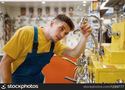 Male builder choosing water tap in hardware store. Constructor in uniform look at the goods in diy shop