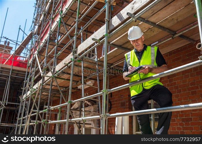 Male builder foreman, construction worker, contractor or architect on building site writing on black clipboard