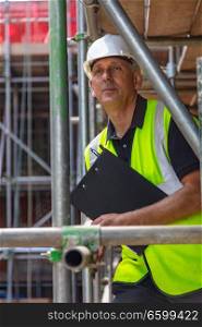 Male builder foreman, construction worker or site manager holding a clipboard, wearing a white hard hat and hi vis vest
