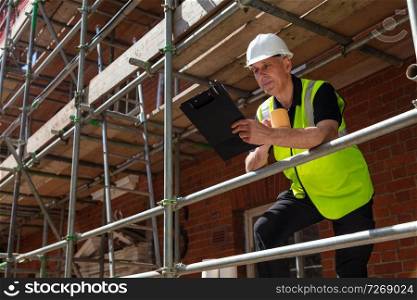 Male builder foreman, construction worker or site manager holding a clipboard, wearing a white hardhat and hi vis vest