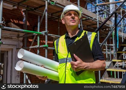 Male builder foreman, worker, surveyor, engineer or architect on construction site holding building plans and clipboard