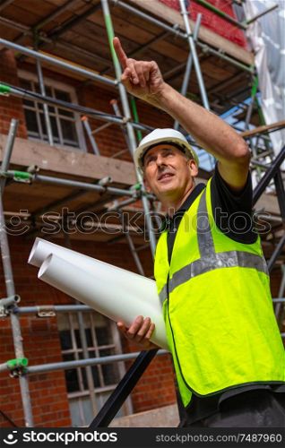 Male builder foreman, worker surveyor, engineer or architect on construction site holding building plans and pointing