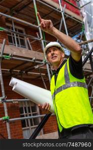Male builder foreman, worker surveyor, engineer or architect on construction site holding building plans and pointing