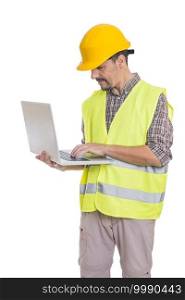 Male builder in helmet and reflective vest standing on white background and browsing netbook. Male engineer in hardhat using laptop