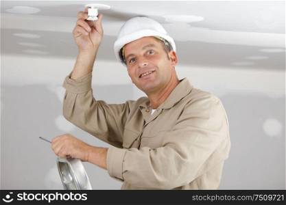 male builder in with helmet installing a light bulb