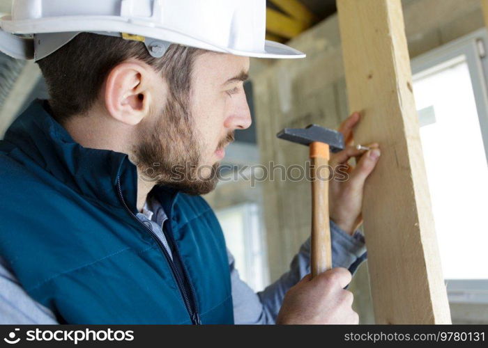 male builder knocking nail into wall with hammer