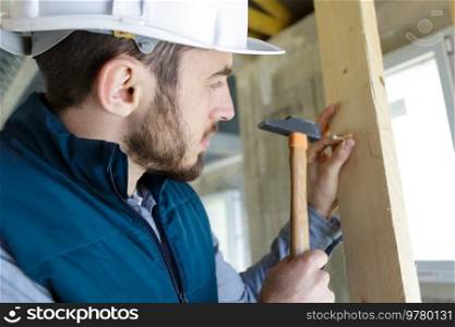 male builder knocking nail into wall with hammer