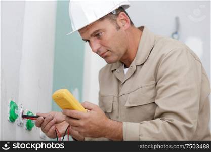 male builder measuring voltage in electrical wall